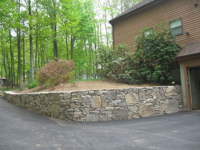 A stone wall surrounds a driveway in front of a house.