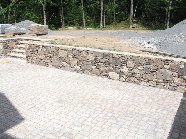 A stone wall surrounds a brick patio with stairs leading up to it.