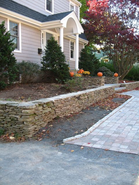 A house with a stone wall and pumpkins in front of it