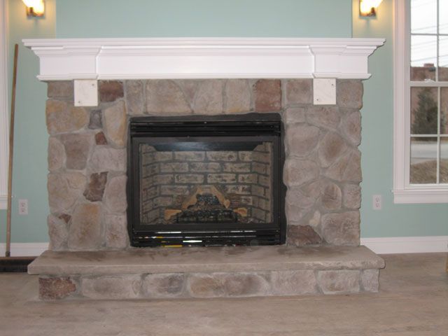 A stone fireplace in a living room next to a window