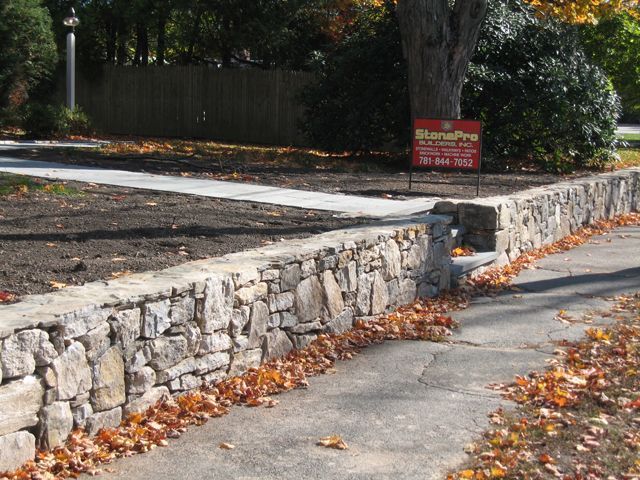 A stone wall along a sidewalk with leaves on it
