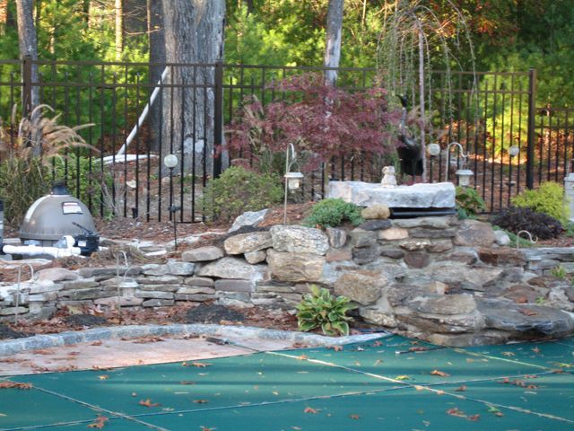 A fence surrounds a swimming pool surrounded by rocks and trees