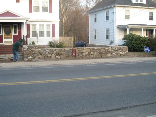 A man is working on a stone wall in front of a house