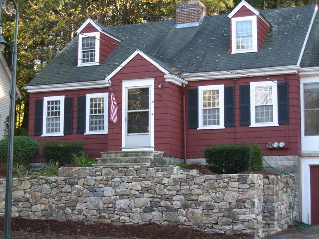 A red house with black shutters and a stone wall