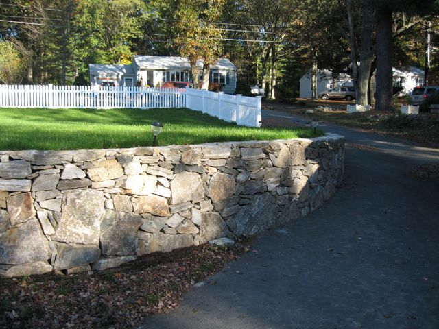 A stone wall with a white picket fence in the background