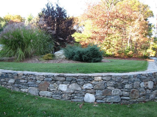 A stone wall surrounds a lush green lawn with trees in the background.