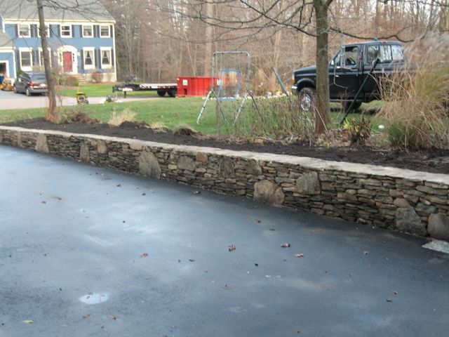 A black truck is parked in a driveway next to a stone wall