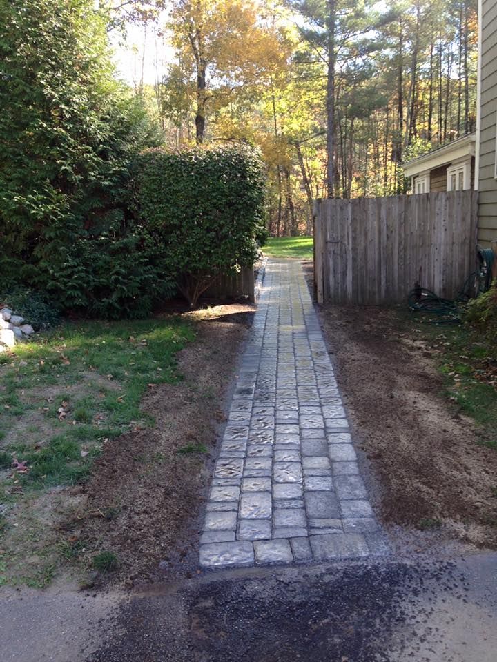 A stone walkway leading to a house with a wooden fence.