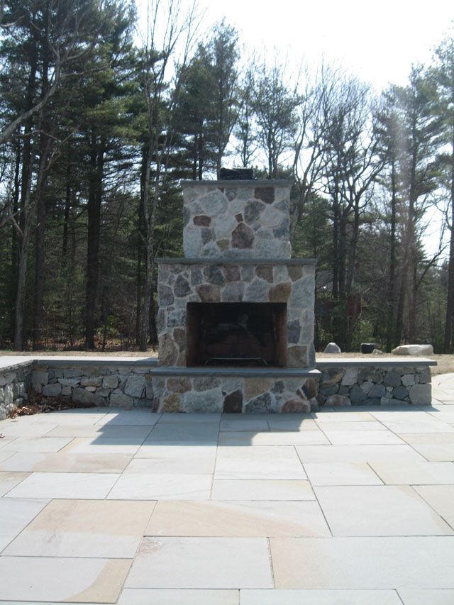 A stone fireplace is surrounded by trees on a patio
