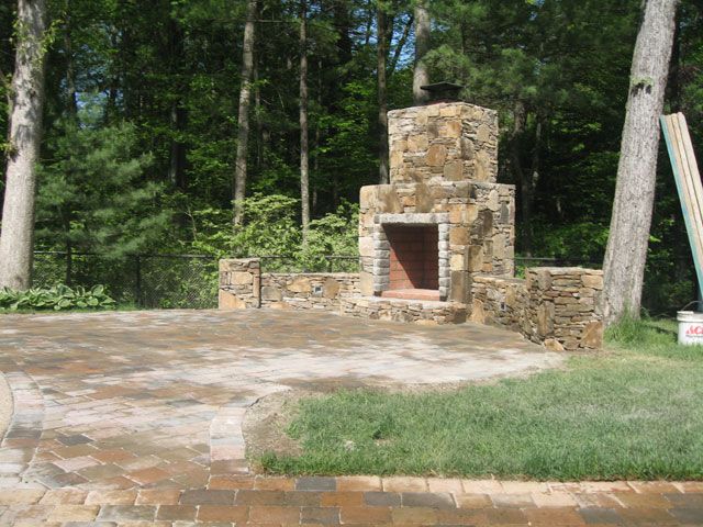 A stone fireplace in the middle of a lush green forest