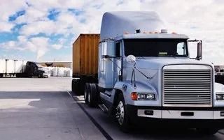 Red semi-truck with a white trailer driving on a highway.