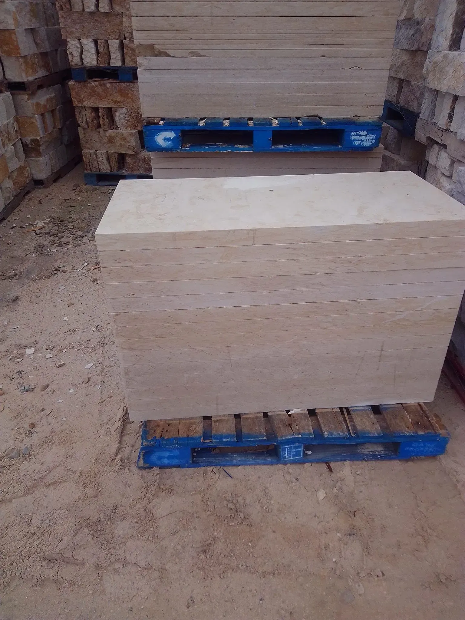 Stacks of beige stone slabs on blue pallets in a storage area.