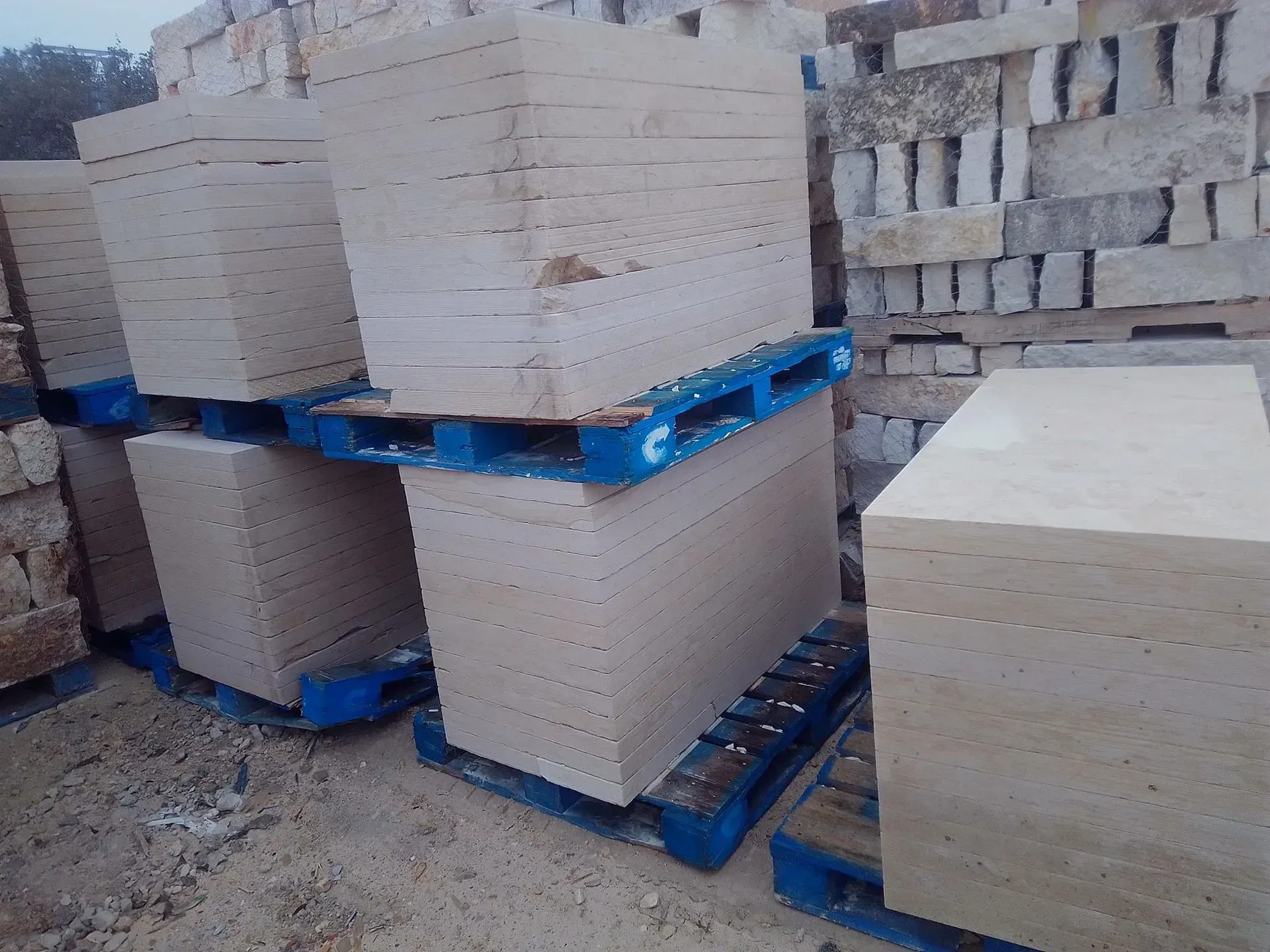 Stacks of rectangular, light-colored stone blocks on blue pallets, outdoors.