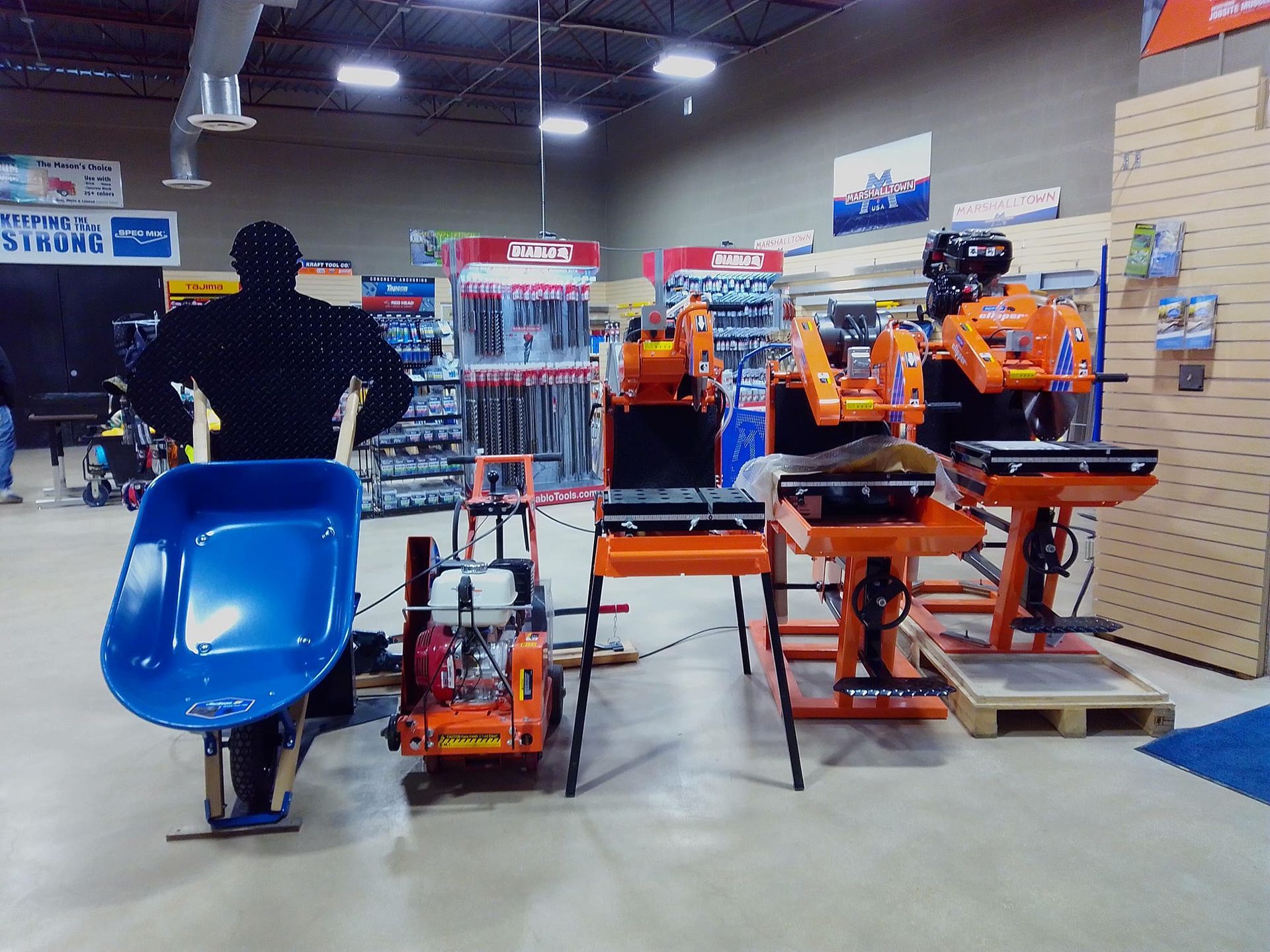 A display of tile saws, a wheelbarrow, and other tools in a hardware store.