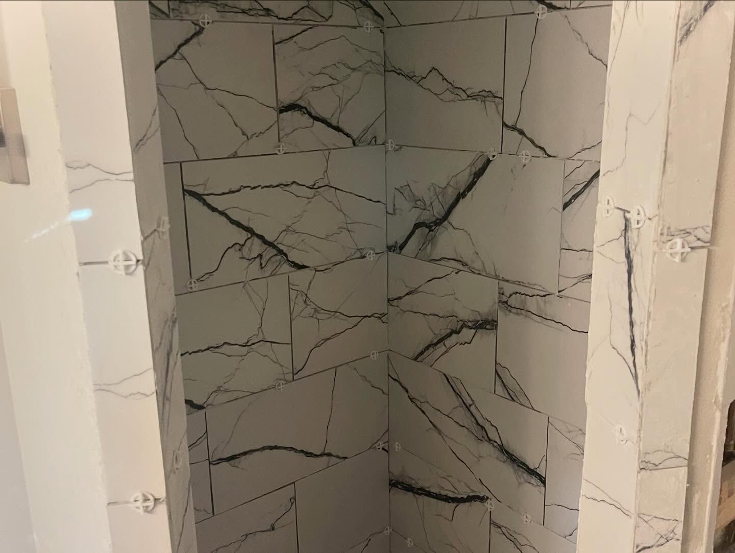A bathroom with marble tiles and a shower stall.
