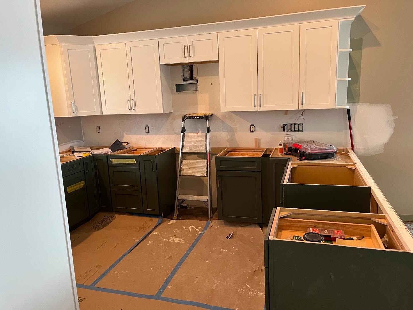 A kitchen under construction with white cabinets and green cabinets.