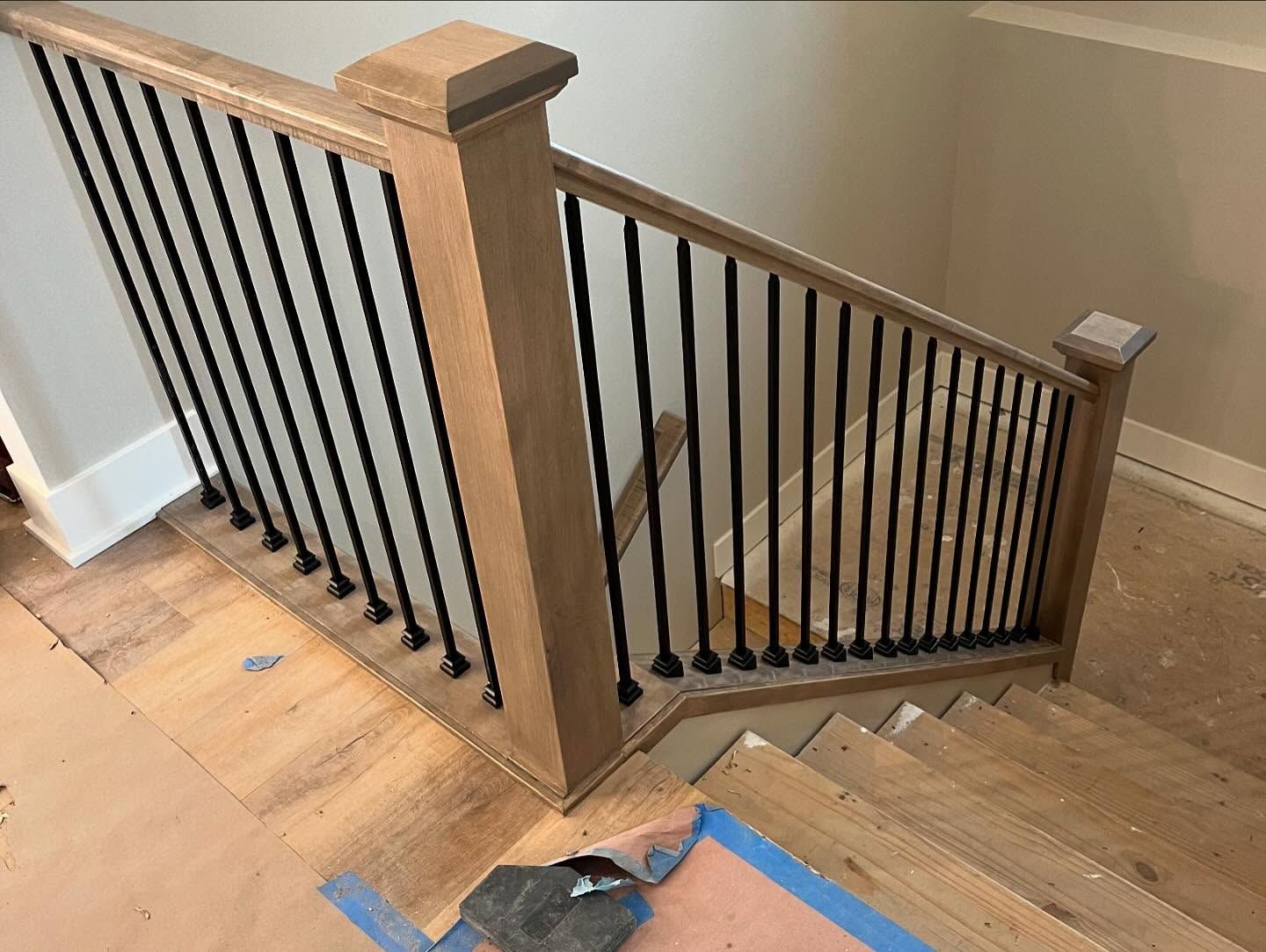 A wooden staircase with a black railing is being built in a house.