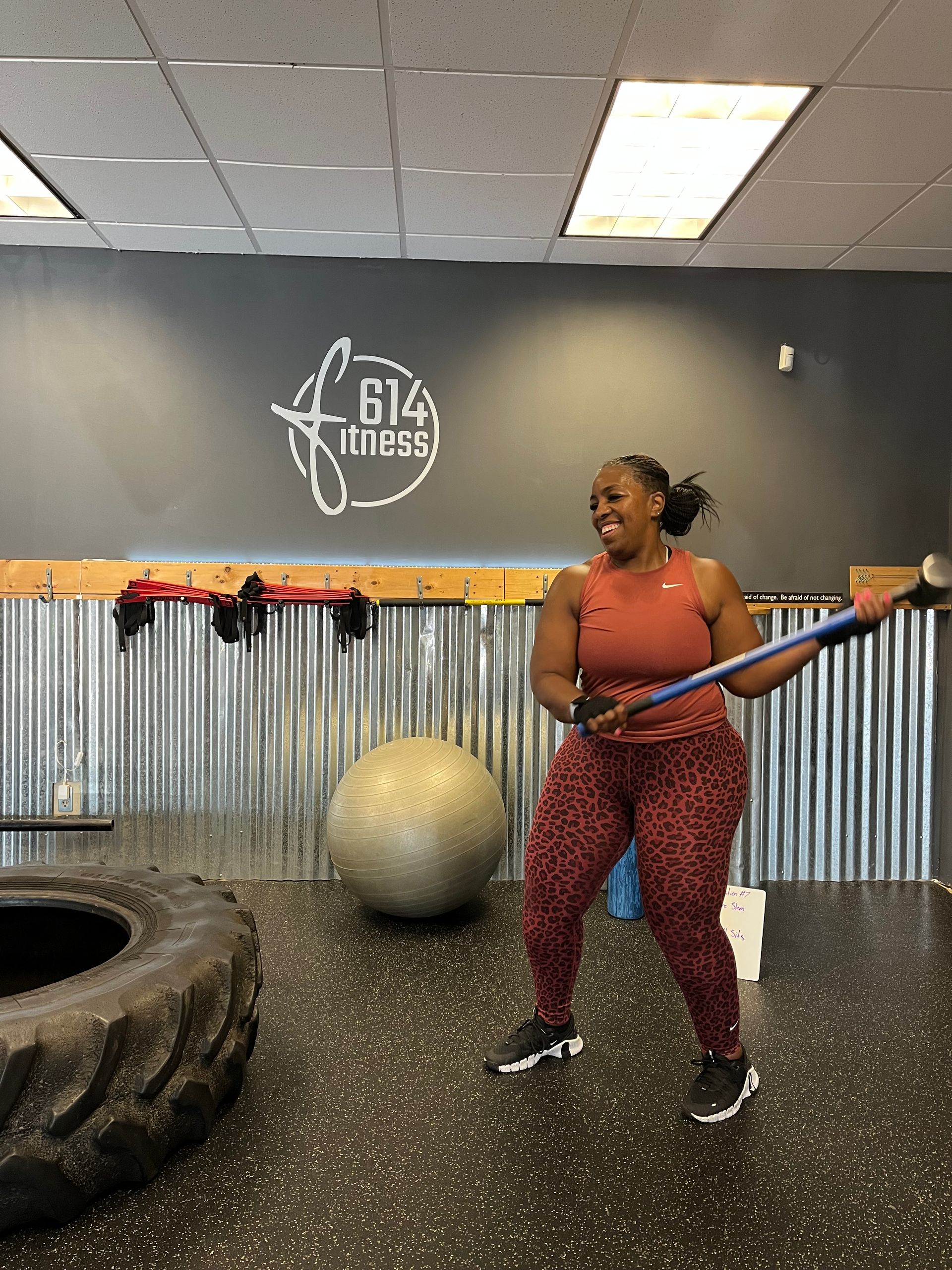 Woman in workout gear swinging a sledgehammer at a tire in a gym.