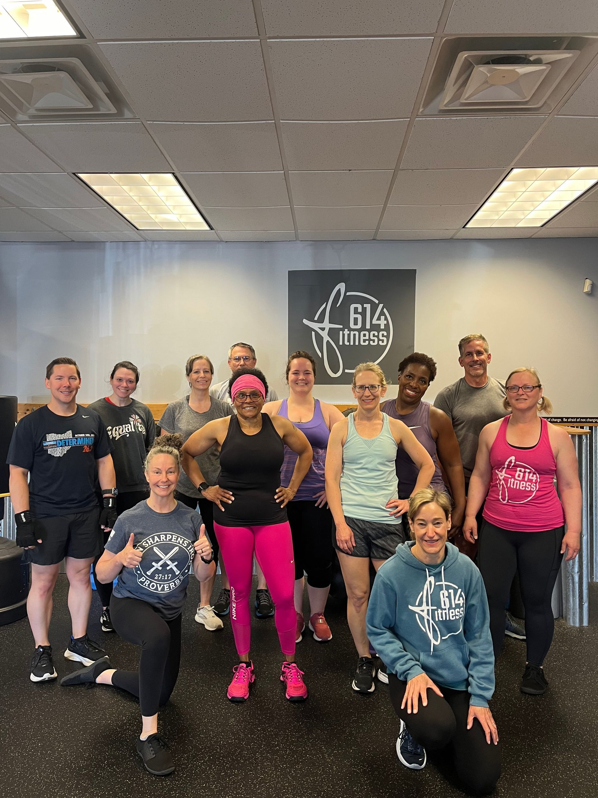 Group of people in fitness attire pose in a gym. The sign 