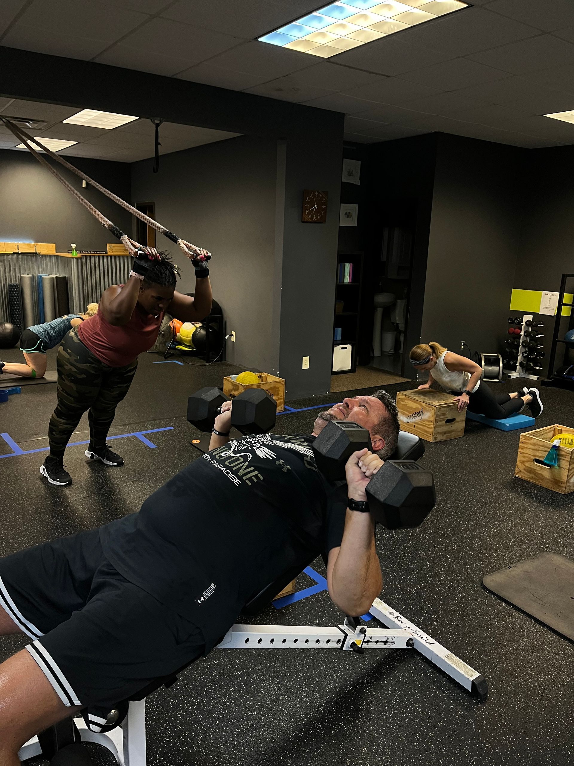 Man lifting dumbbells on a weight bench. Other people workout in a gym.