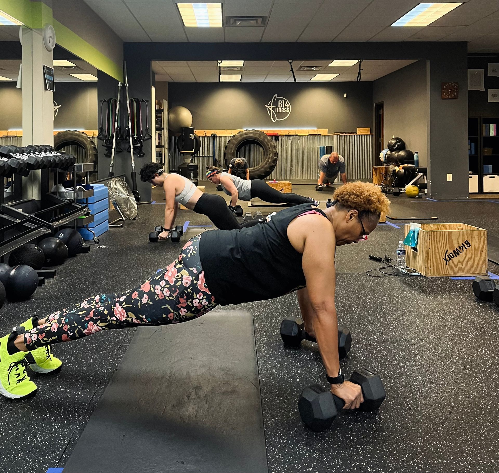People exercising indoors, doing pushups with dumbbells on a gym floor.