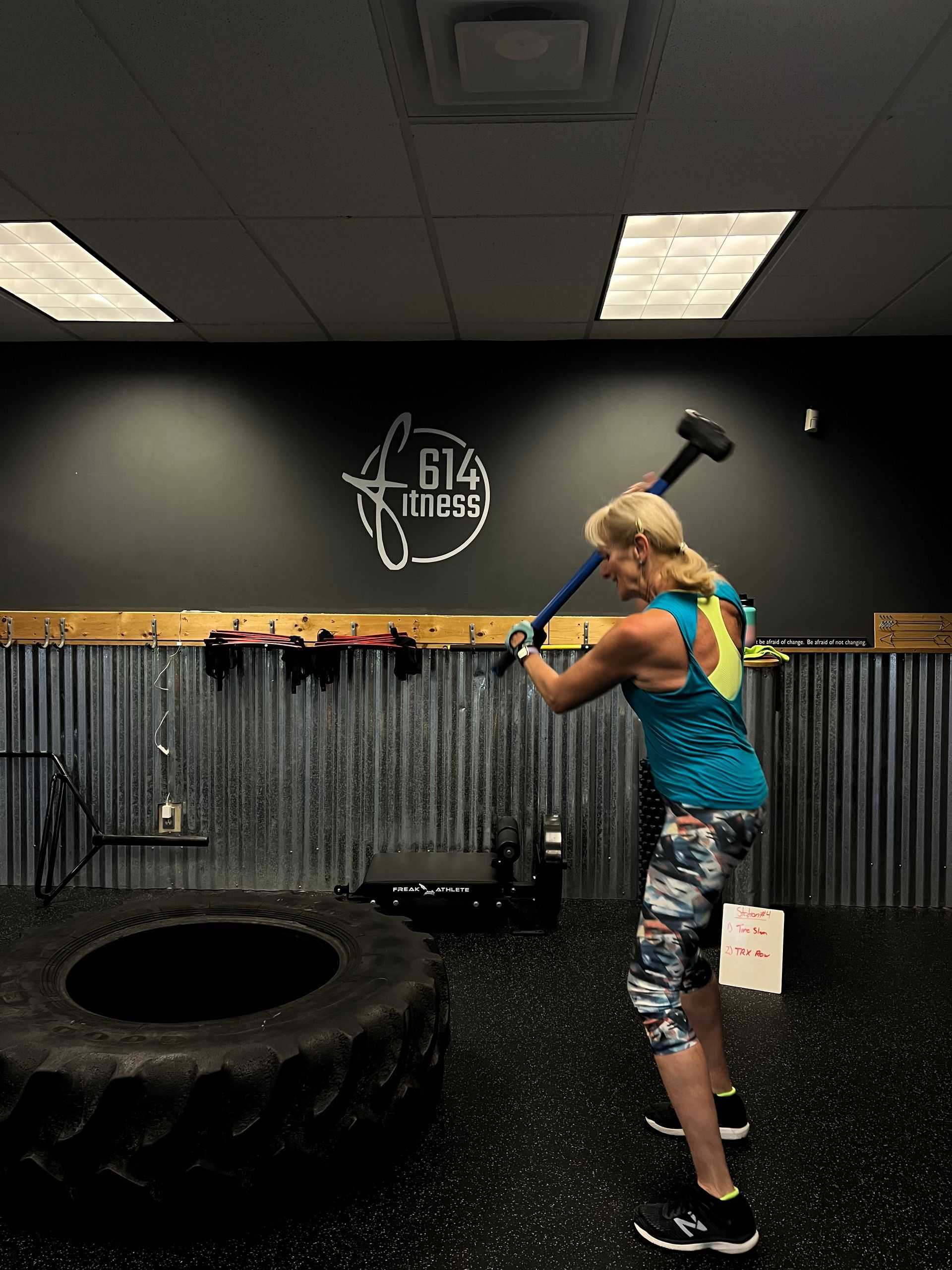 Woman swinging a sledgehammer at a tire in a gym.