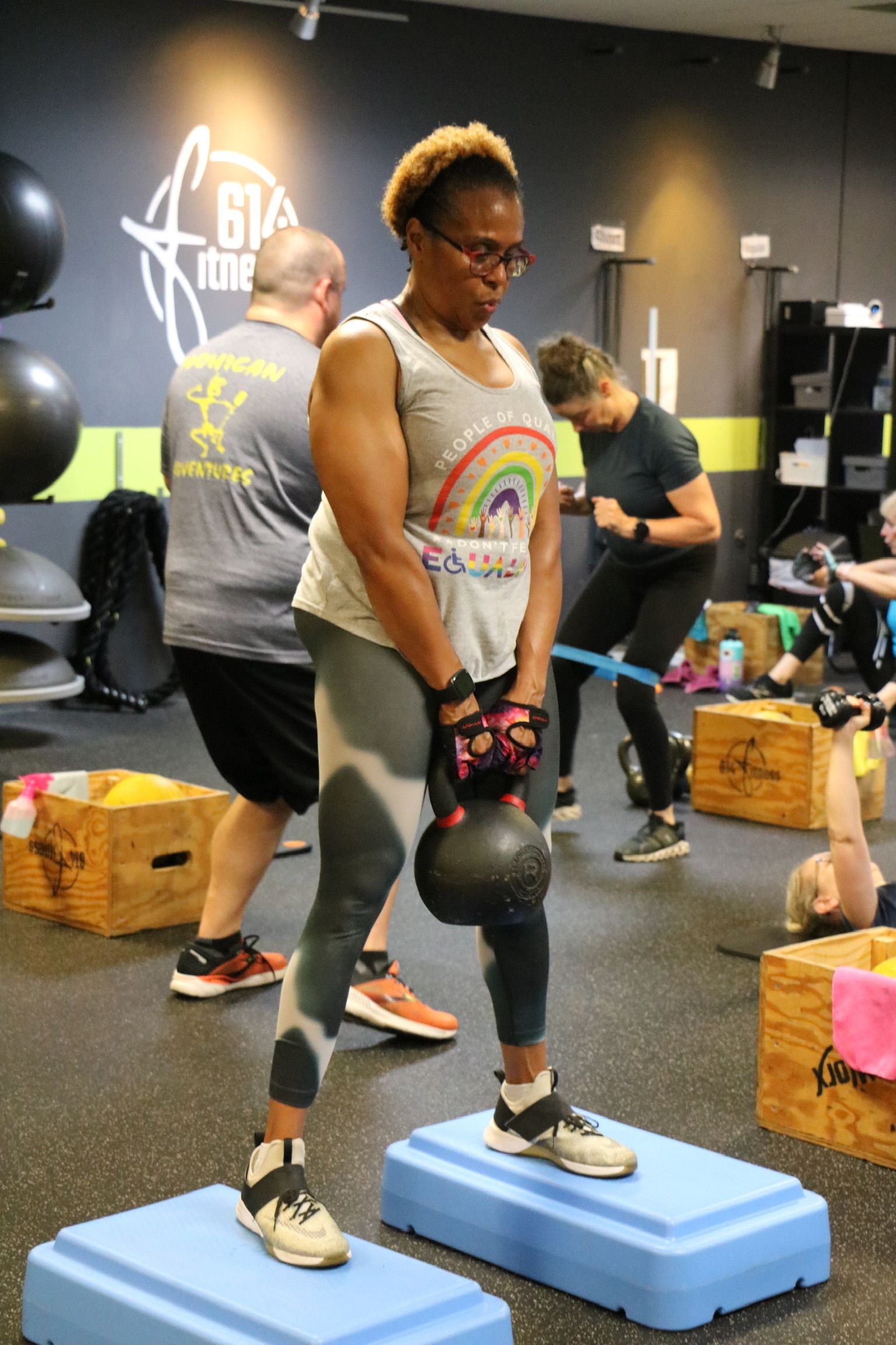 Woman in gym lifts kettlebell while standing on step platforms.