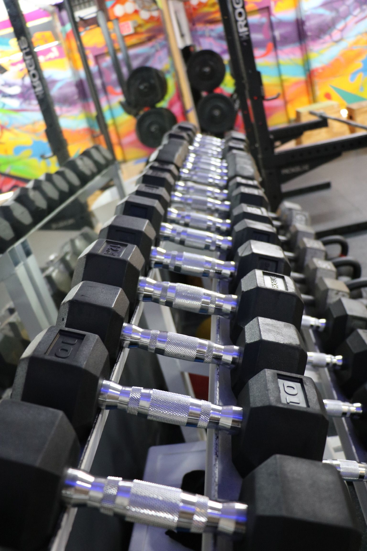 Dumbbell rack in a gym with weights, rows and a colorful graffiti background.