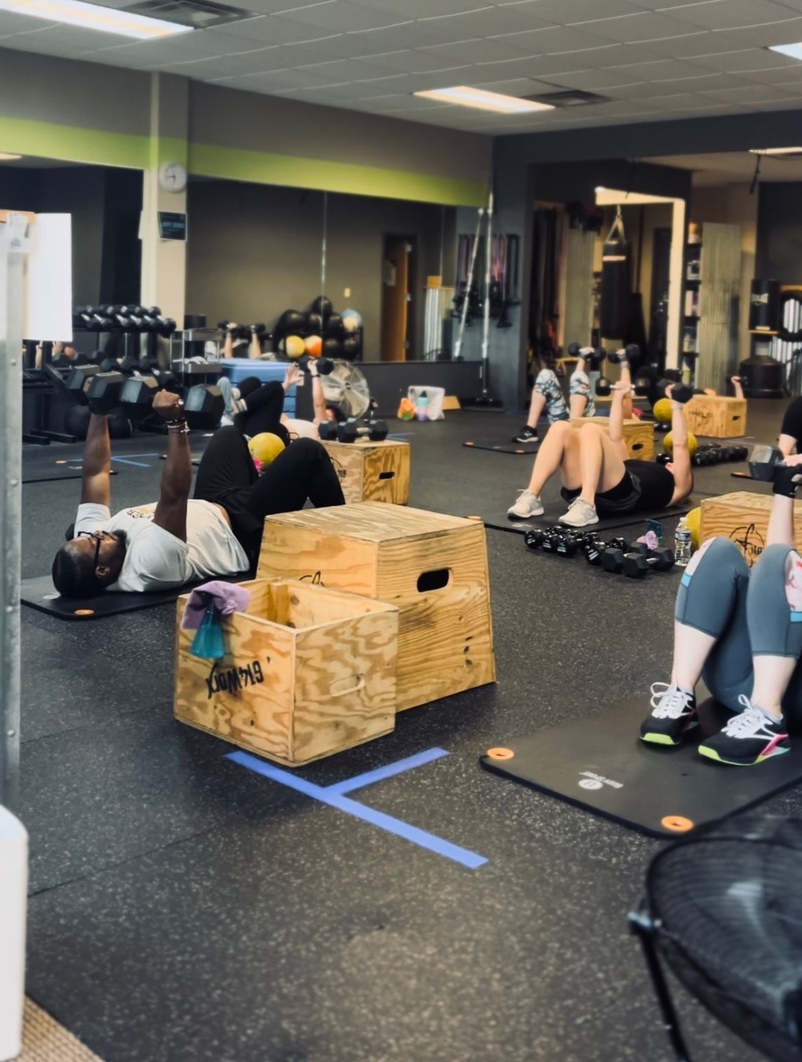 People exercising on mats in a gym.  They are using weights and boxes.