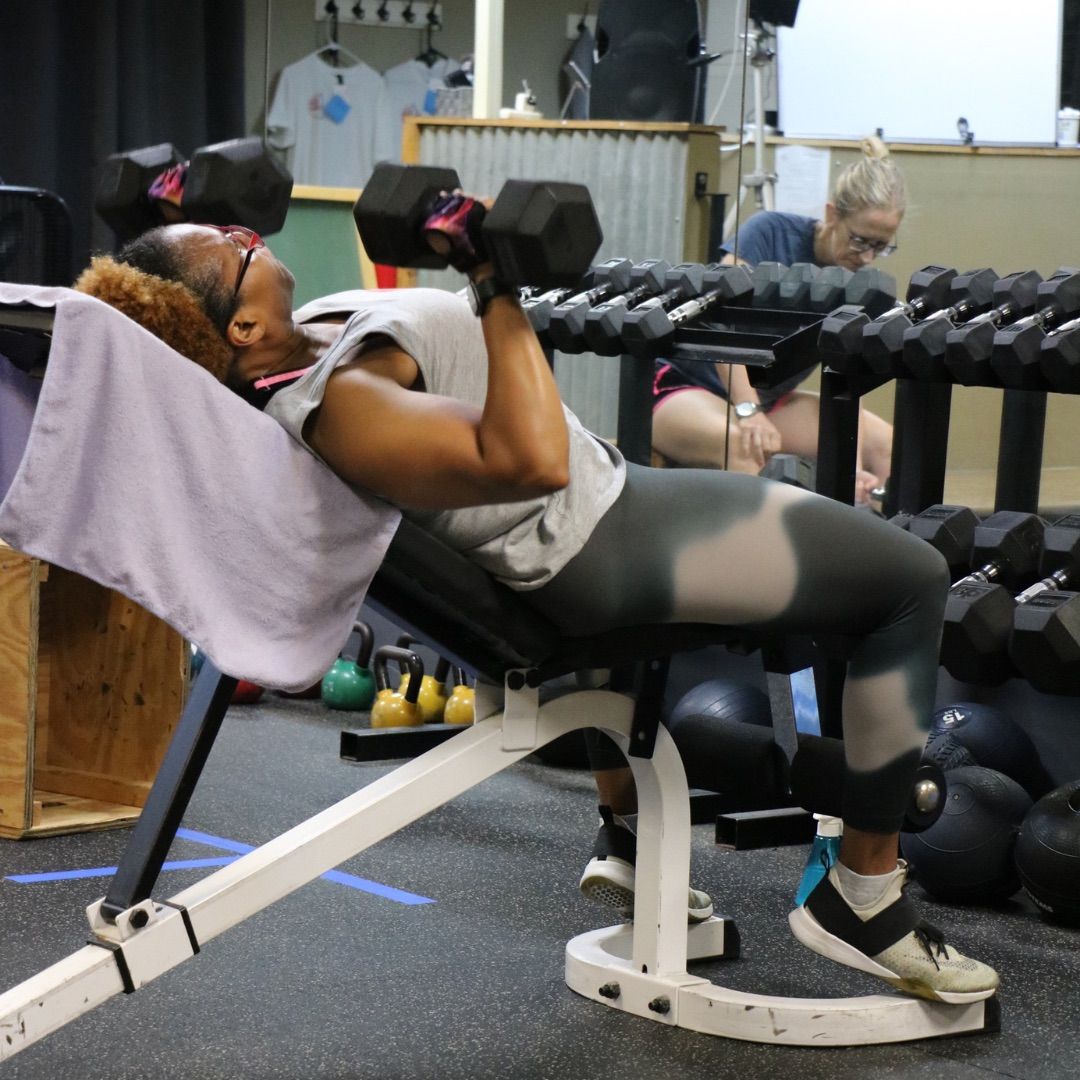 Person using dumbbells on an incline bench in a gym.