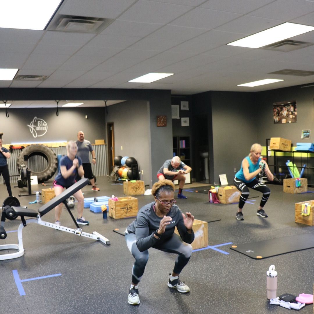 People exercising in a gym: squatting, lunging, and using equipment. Gray walls and flooring.