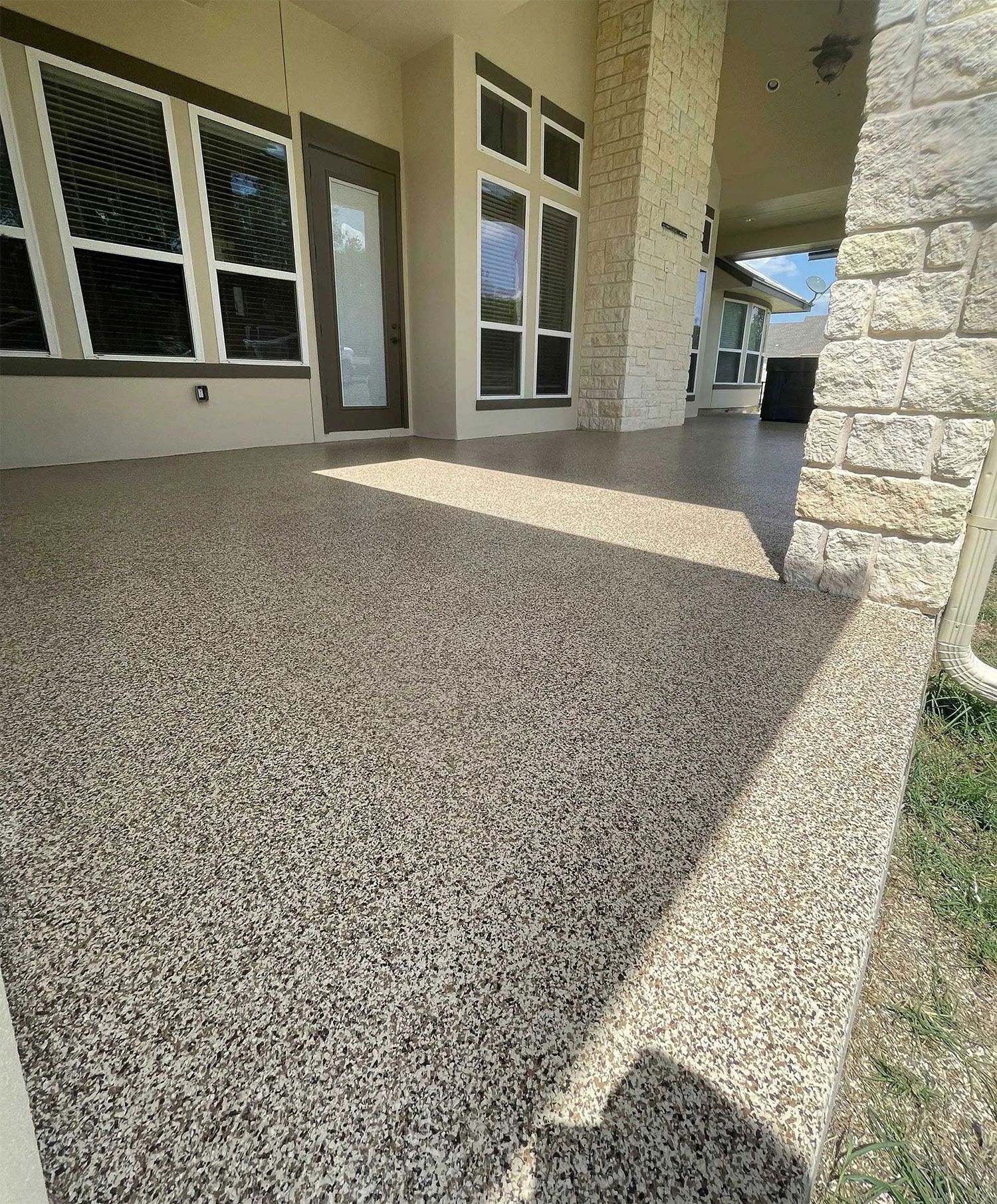 Covered porch with speckled flooring, a stone pillar, and windows.