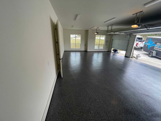 Garage interior with epoxy flooring, white walls, windows, and open garage door to outside.