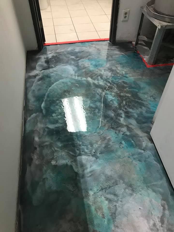 Metallic epoxy floor with blue, gray, and silver swirls, reflecting a light fixture.