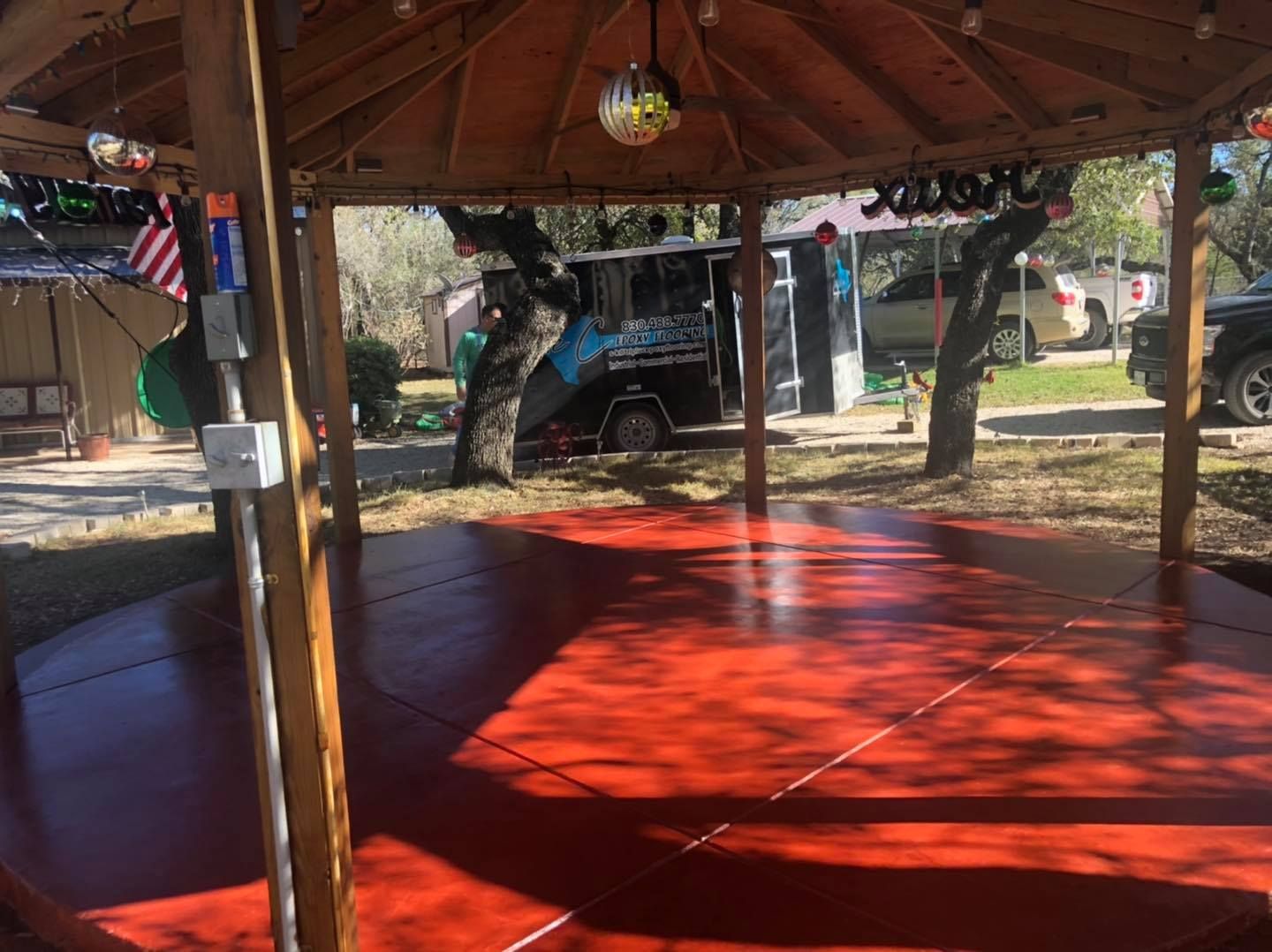 Red-floored outdoor gazebo with disco ball, string lights, and food truck in background.