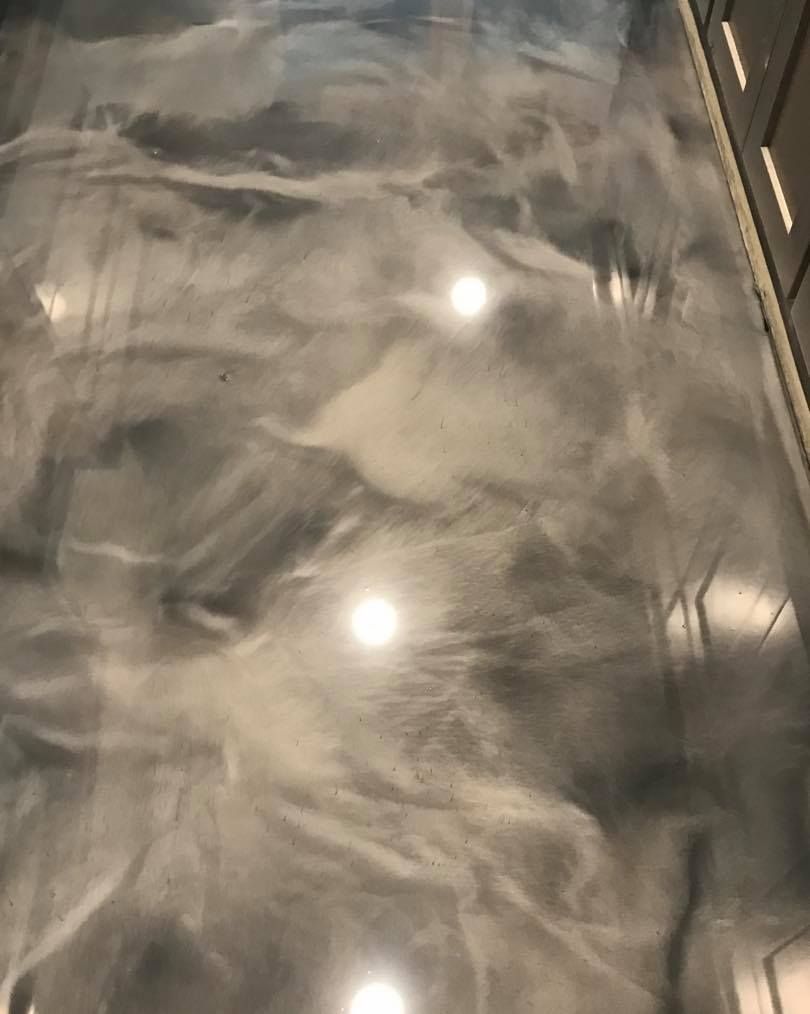 Metallic epoxy flooring with flowing silver and gray patterns, reflecting overhead lights.
