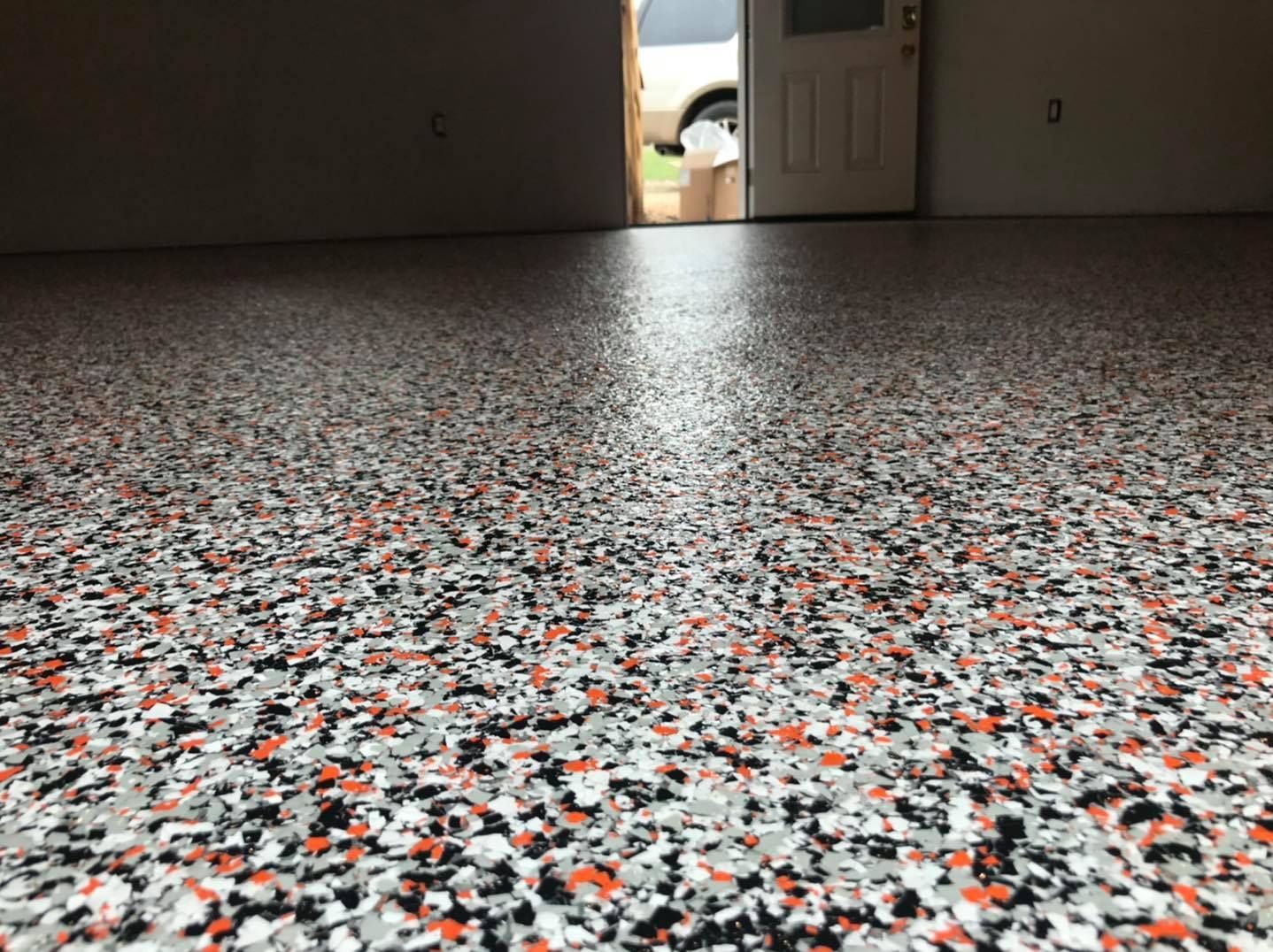 Close-up view of a shiny speckled epoxy floor with orange, black, and gray chips, garage setting.