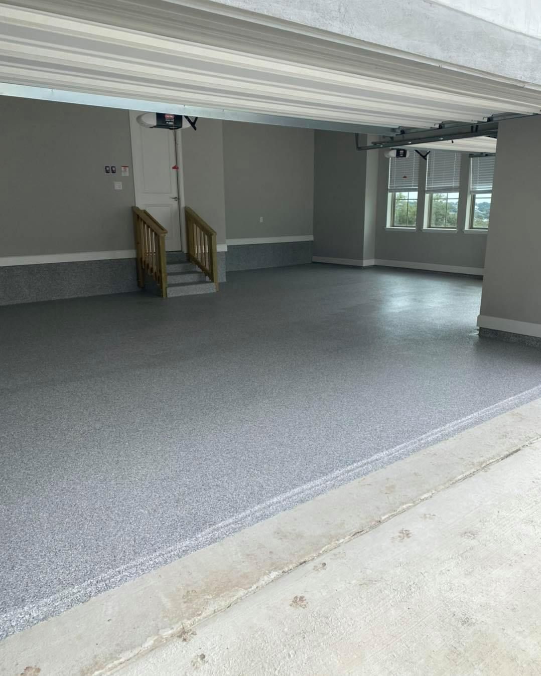 A newly painted garage interior with a gray speckled floor. A door and stairs are visible.