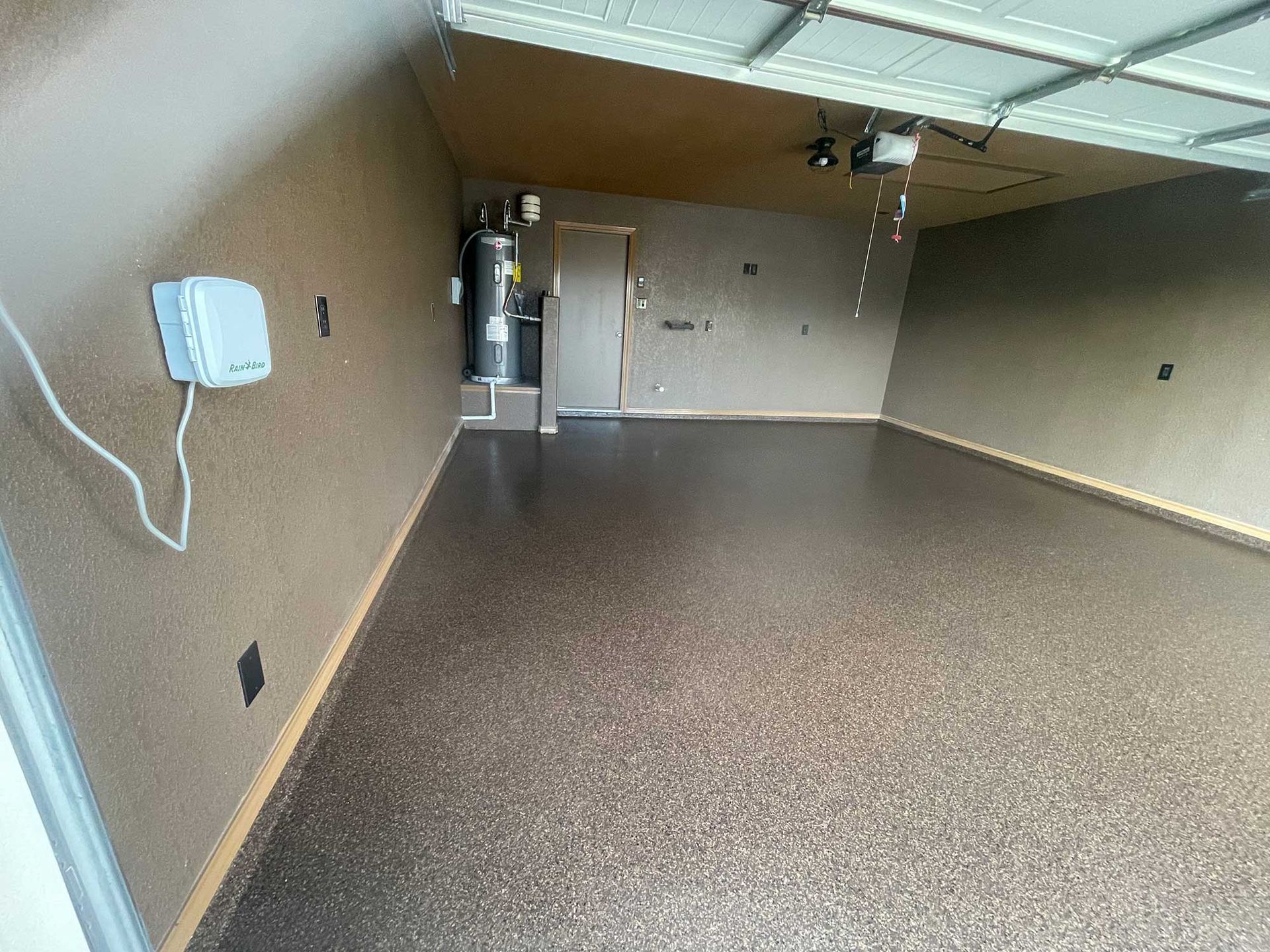 Empty garage with epoxy floor, water heater, and beige walls.