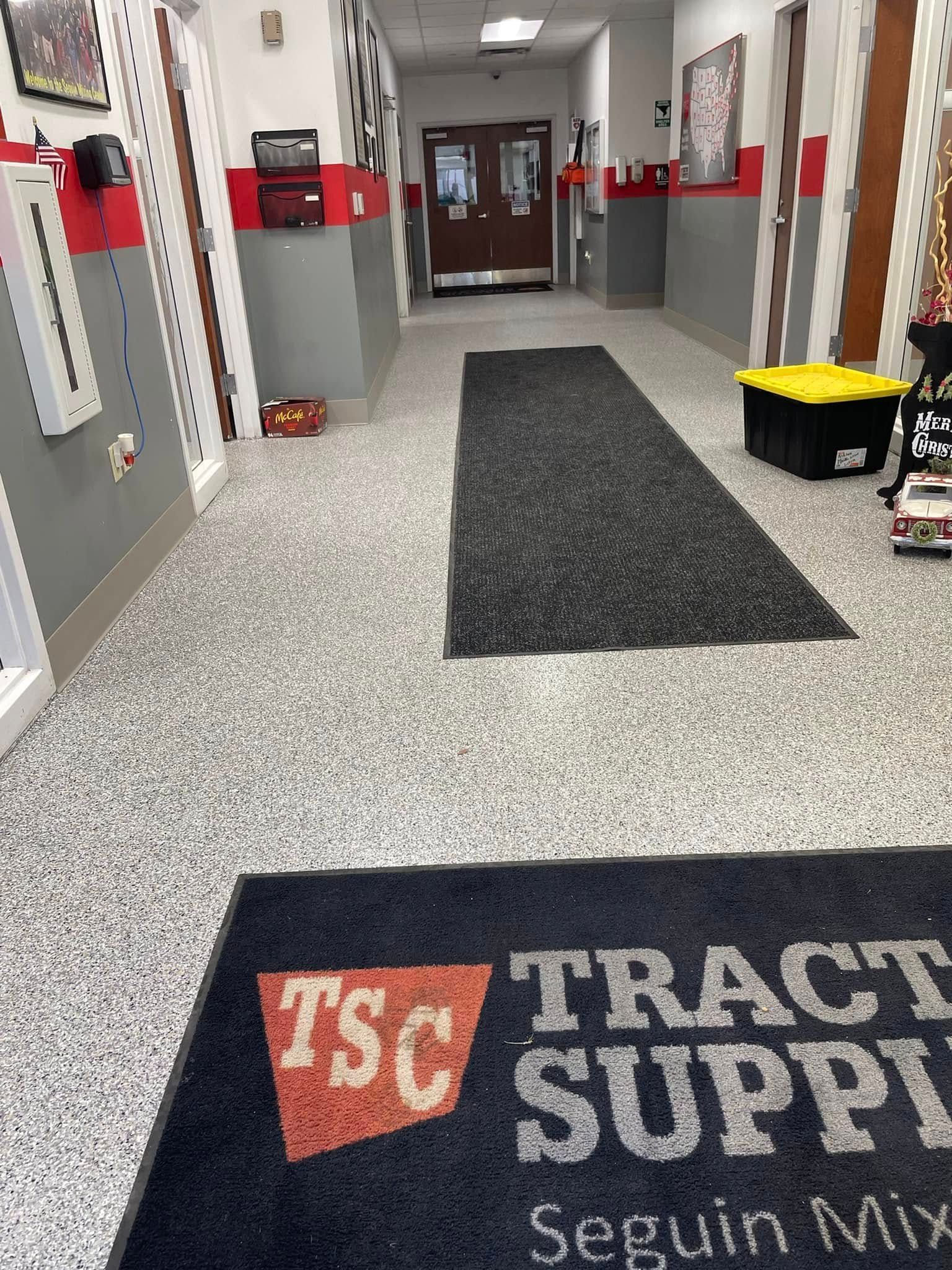 Hallway at Tractor Supply store, featuring a welcome mat, gray speckled floor, and doors.