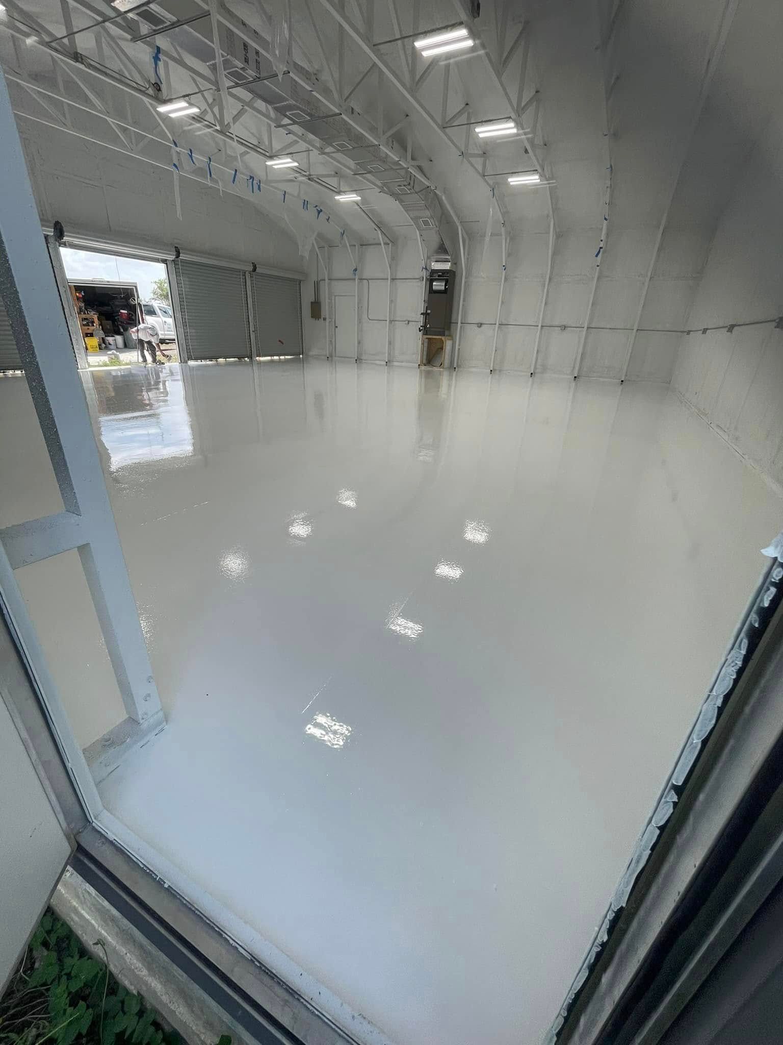 Interior view of a spacious, light gray warehouse with a freshly coated floor and open doors.
