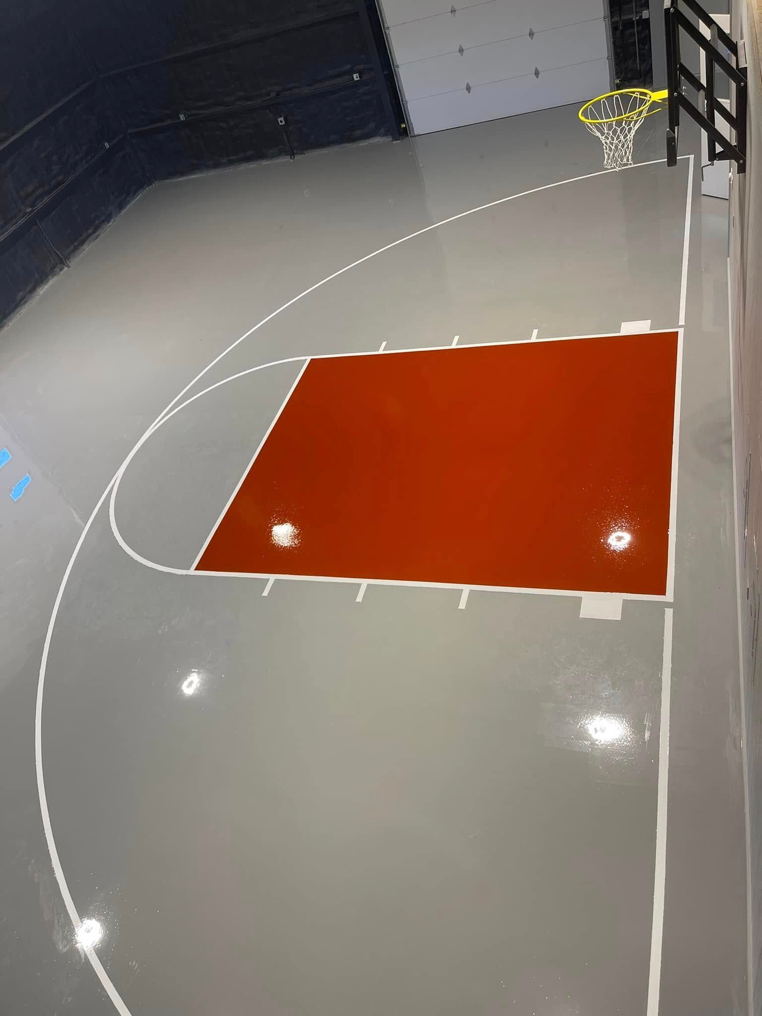 Indoor basketball court with a gray floor, red key, white lines, and a basketball hoop.