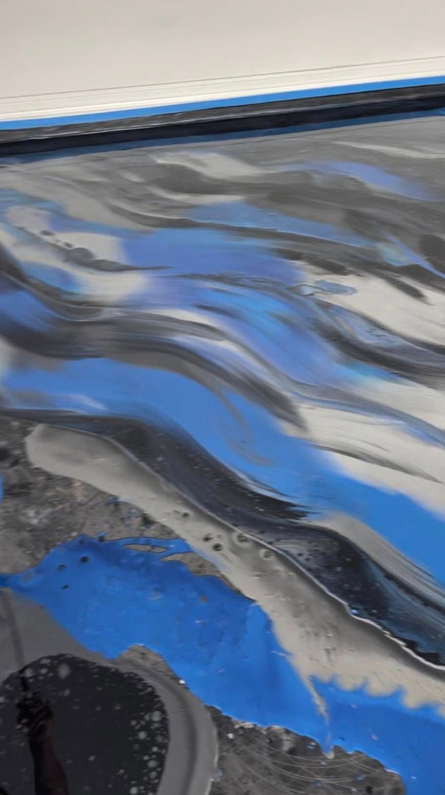 Abstract blue, gray, and black epoxy floor with flowing wave-like patterns.