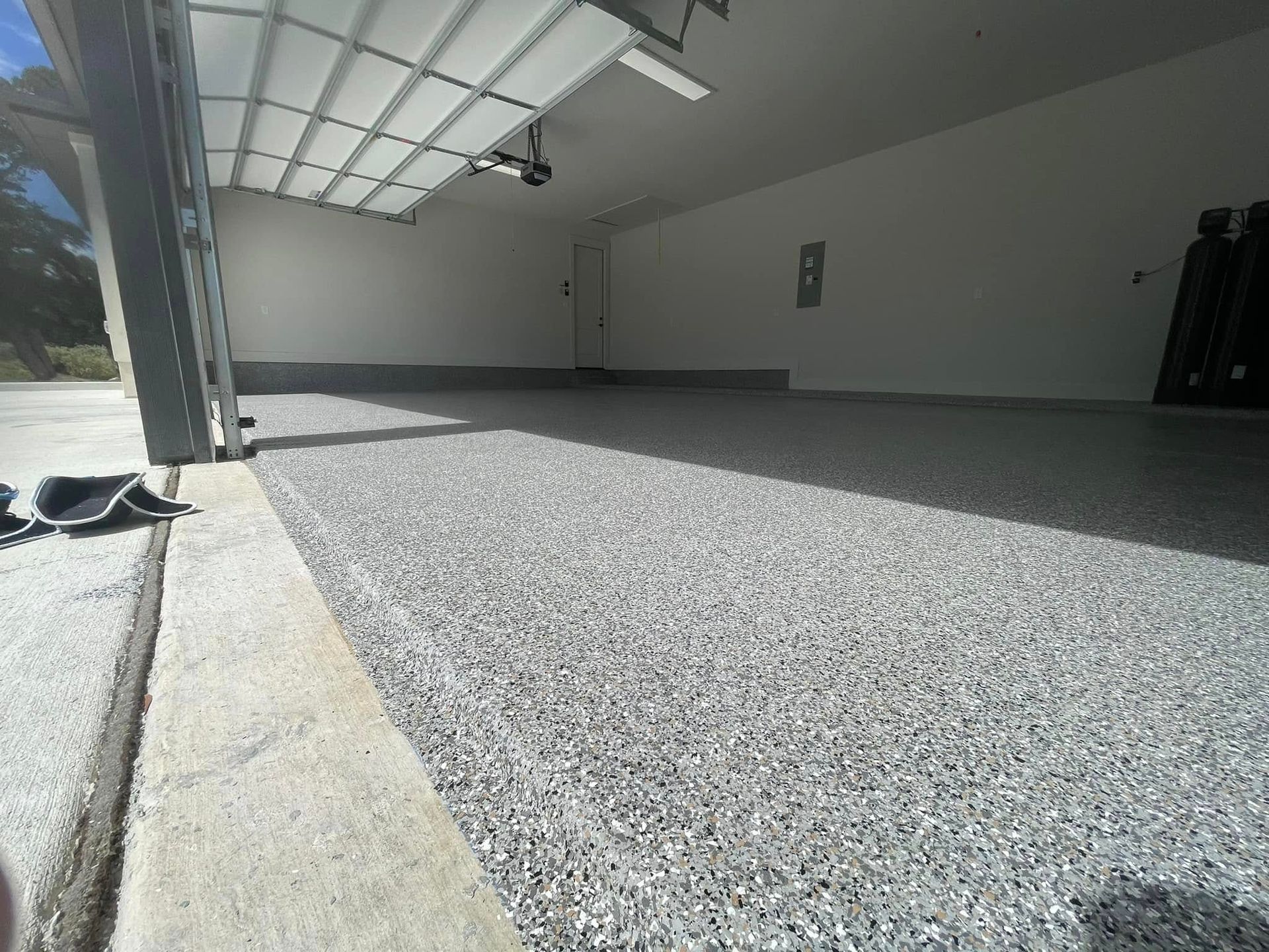 A freshly coated garage floor with gray and white chips. Garage door open. White walls.