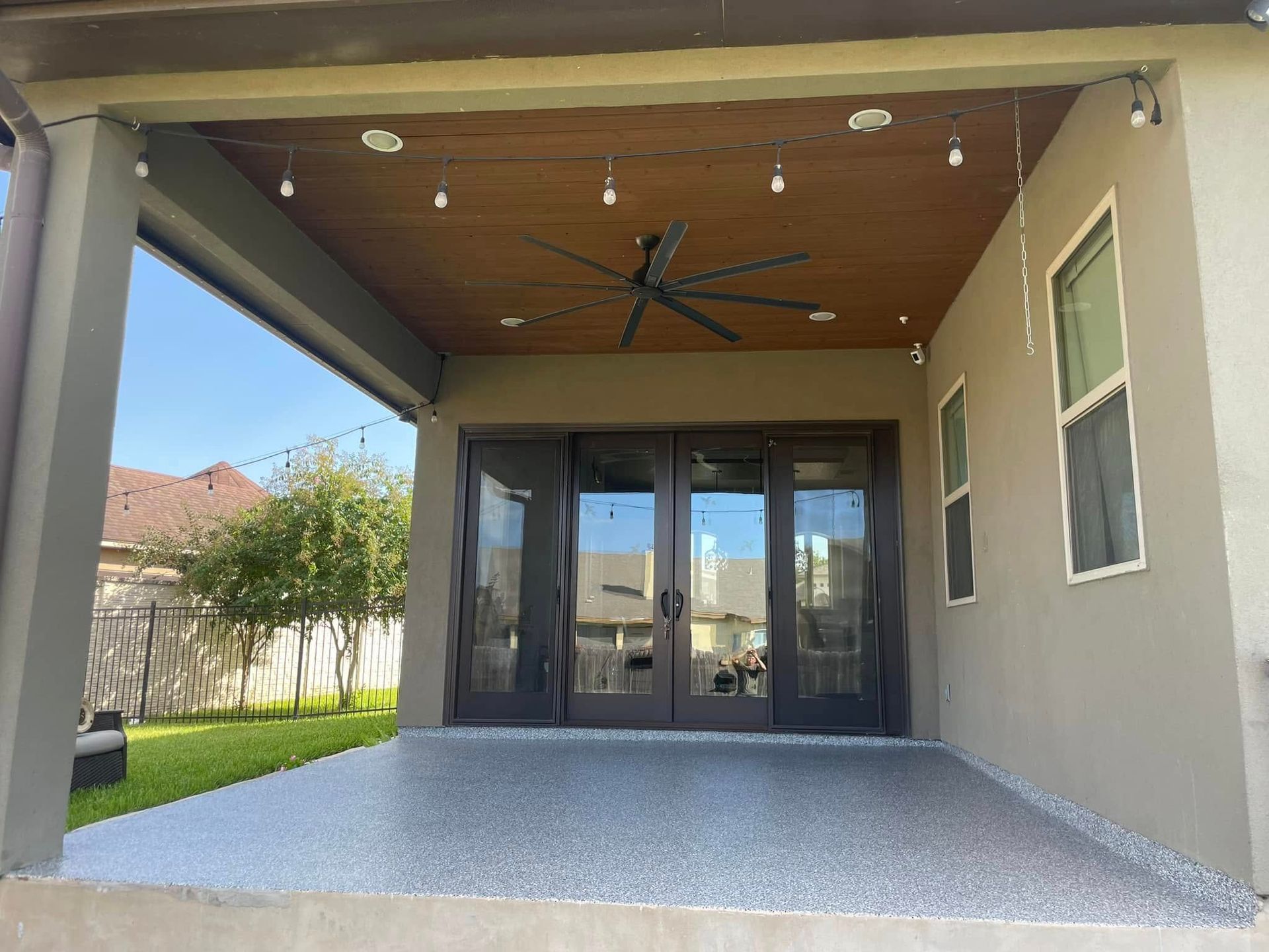 Covered patio with gray floor, dark door, ceiling fan, string lights.