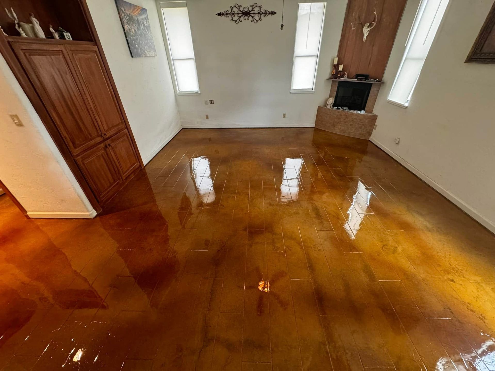 Golden epoxy floor in a room with white walls, windows, and fireplace. Brown cabinets and a painting on the wall.