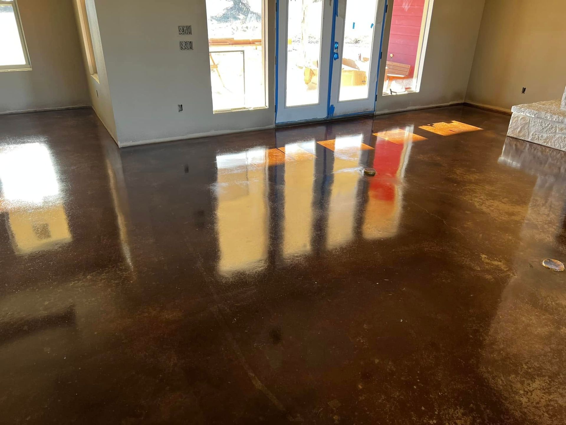 Polished brown concrete floor reflecting sunlight from windows, in a room under construction.
