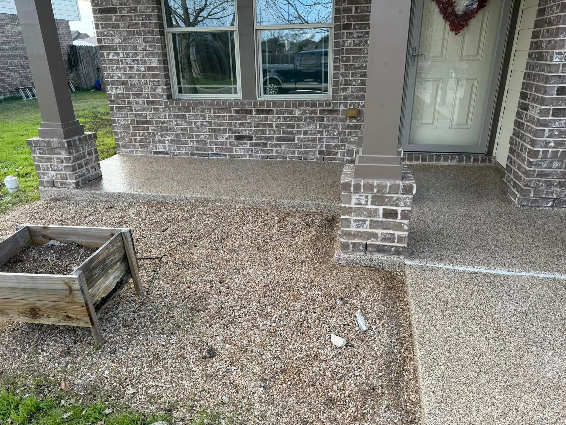 Front porch with stone aggregate, brick columns, and a wooden planter.