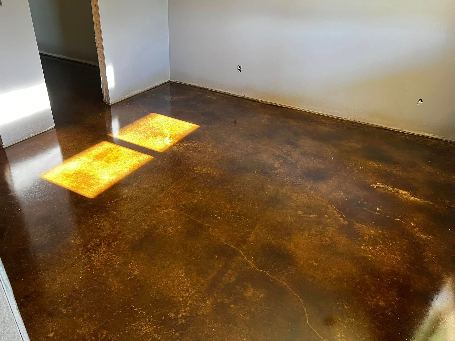 Polished brown and gold concrete floor reflecting sunlight in a room with white walls.