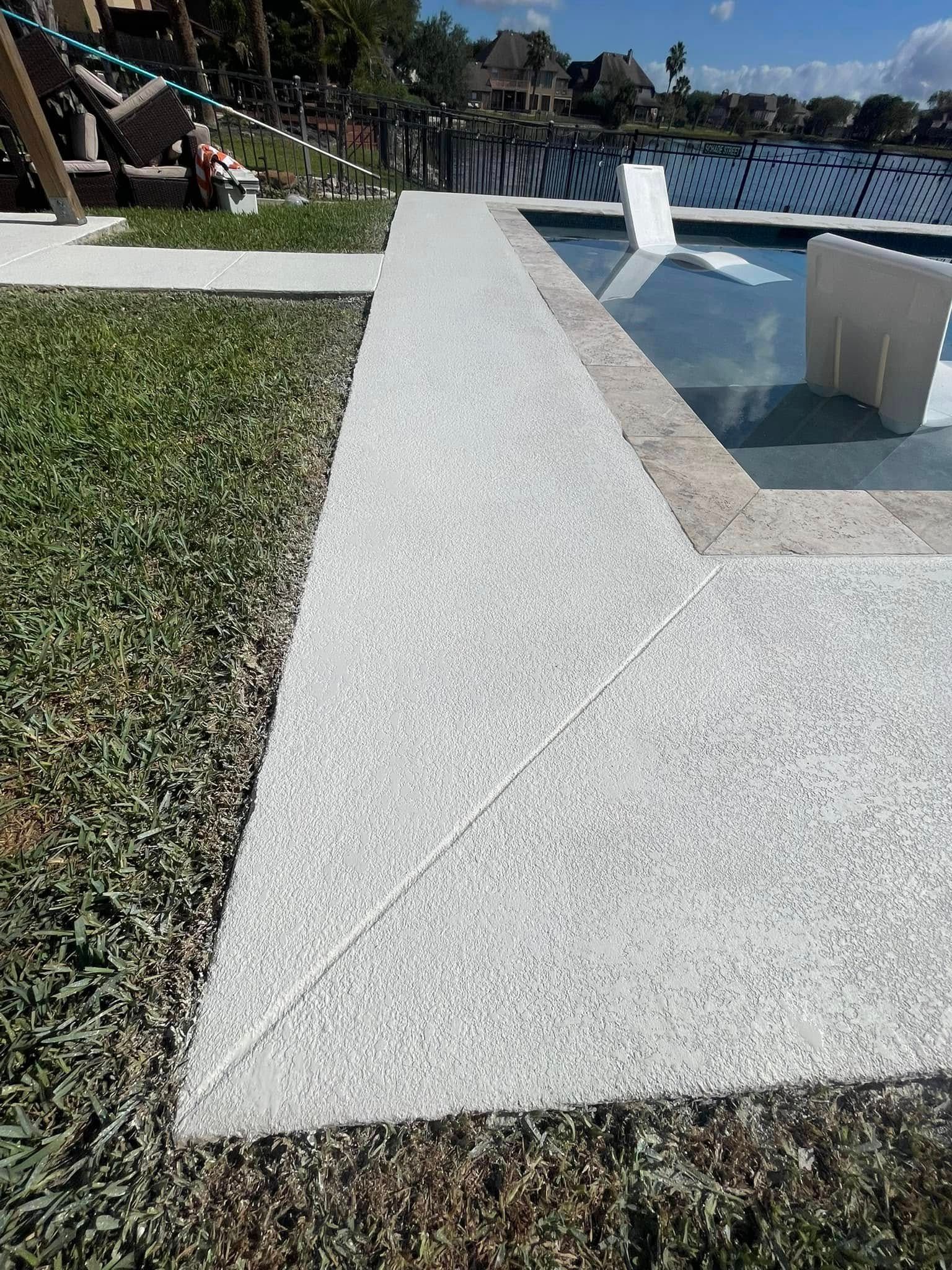 White speckled concrete pathway beside green grass and a swimming pool.